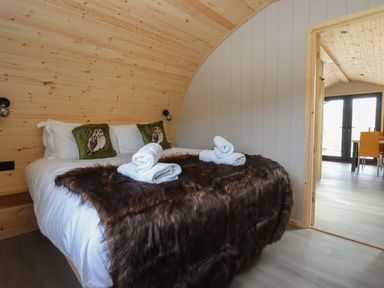 A bedroom with a bed with owl pillows and rolled towels on a brown blanket and an open door looking into a room with a table and chairs at Barn Owl in Chapel Le Dale near Ingleton