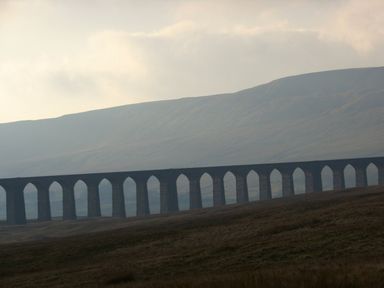 A stone viaduct with multiple arches across a grassy landscape with hills in the background at Barn Owl Chapel Le Dale near Ingleton