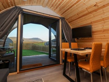 A wooden interior room with orange chairs around a table and a mounted television at Barn Owl in Chapel Le Dale near Ingleton