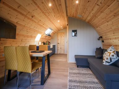 A small wooden room with a dining table and yellow chairs a gray sofa with cushions and a kitchen area at Barn Owl Chapel Le Dale near Ingleton