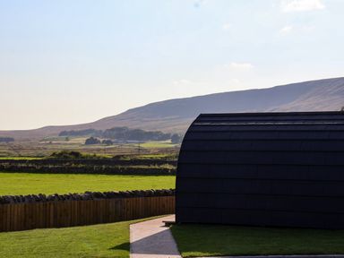 A curved black structure with a path and grass in a rural landscape with hills at Barn Owl in Chapel Le Dale near Ingleton