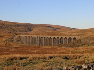 A stone railway viaduct crossing a dry grassy valley with hills in the background at Curlew in Chapel Le Dale near Ingleton