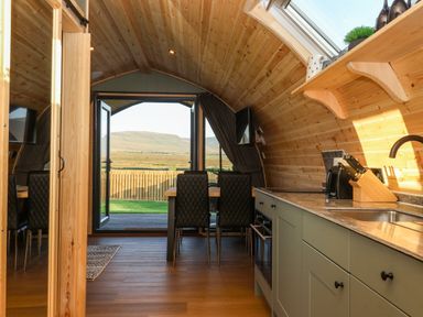 A kitchen and dining area with wooden walls and ceiling and a view of hills through open doors at Curlew in Chapel Le Dale near Ingleton