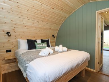 A bedroom with a wooden bed frame white bedding rolled towels and a green wall panel at Curlew in Chapel Le Dale near Ingleton