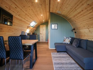 An arched wooden room with a dining table with black chairs a gray sectional sofa and a kitchen area at Woodpecker in Chapel Le Dale near Ingleton