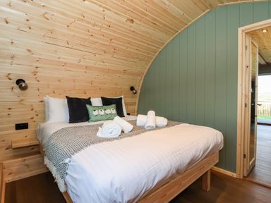 A bedroom with a double bed with rolled towels and pillows against a wooden wall at Woodpecker in Chapel Le Dale near Ingleton