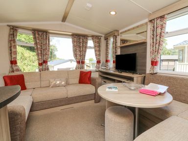 A living room with beige sofas and a round table with a television and patterned curtains at 25 Manleigh Park in Combe Martin