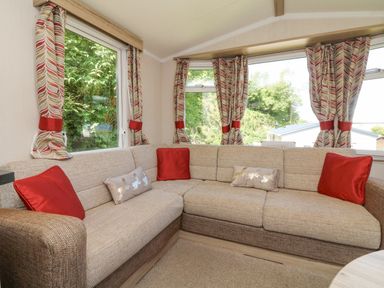 A corner sofa with red and beige cushions by windows with patterned curtains at 25 Manleigh Park in Combe Martin