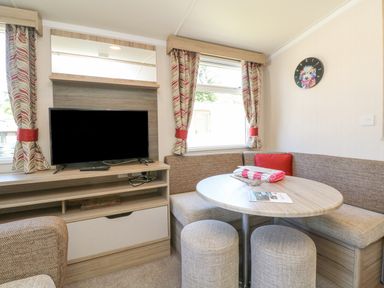A small dining area with a round table seats and a television on a wooden cabinet at 25 Manleigh Park in Combe Martin