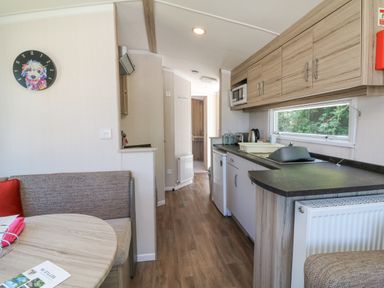 A narrow kitchen and dining area with wooden cabinets a round table and cushioned seating at 25 Manleigh Park in Combe Martin