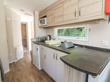 A kitchen with cabinets a microwave a small fridge a sink and a window at 25 Manleigh Park Combe Martin