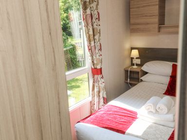 A small bedroom with a single bed towels on the bed near a window with patterned curtains at 25 Manleigh Park Combe Martin