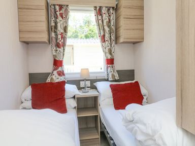 A bedroom with two single beds red pillows and a small nightstand with a lamp at 25 Manleigh Park in Combe Martin