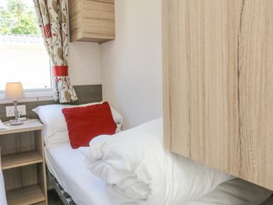 A bedroom with single bed red pillow wooden bedside table lamp and patterned curtains at 25 Manleigh Park Combe Martin