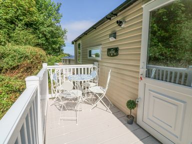 An outdoor patio with a white metal table and four chairs next to a beige mobile home at 25 Manleigh Park in Combe Martin