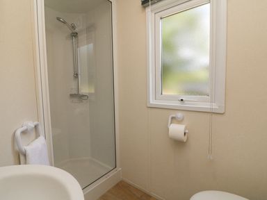 A bathroom with a shower cubicle a toilet paper holder under a frosted window and a hand towel ring at 26 Manleigh Park in Combe Martin