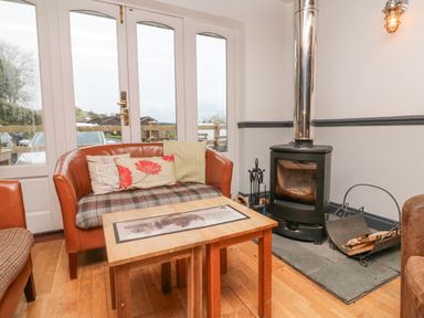 A sitting area with a wooden table two chairs and a wood-burning stove near glass doors at 26 Manleigh Park in Combe Martin