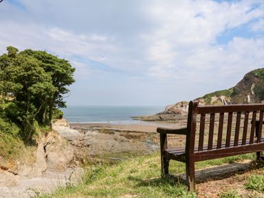 A bench facing a rocky beach with trees on the left and cliffs on the right at 26 Manleigh Park in Combe Martin