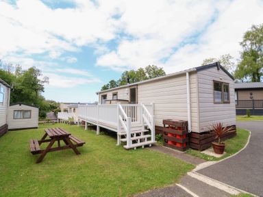 A mobile home with a white railing and steps next to a wooden picnic table on grass at 26 Manleigh Park in Combe Martin