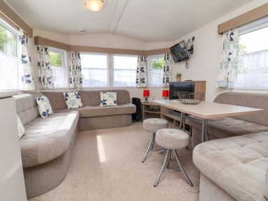 A living room with beige sofas cushions a table stools a wall mounted TV and windows at 26 Manleigh Park in Combe Martin