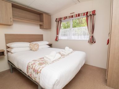 A bedroom with a double bed towels on the bed and a window with curtains at 26 Manleigh Park in Combe Martin