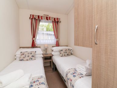 A bedroom with two single beds a window with striped curtains and a wooden wardrobe at 26 Manleigh Park in Combe Martin