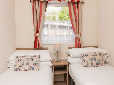 A bedroom with two single beds a nightstand with a lamp and a window with striped curtains at 26 Manleigh Park Combe Martin