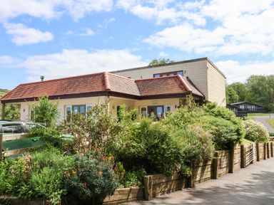 A house with a red tiled roof surrounded by greenery and a wooden fence at 26 Manleigh Park in Combe Martin