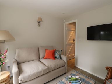 A living room with a beige sofa and two cushions a wall-mounted tv and a door at Little Robin Cottage in Ambleside