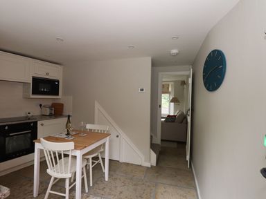 A kitchen with a small dining table and two chairs next to a staircase and an open door leading to a living area at Little Robin Cottage in Ambleside