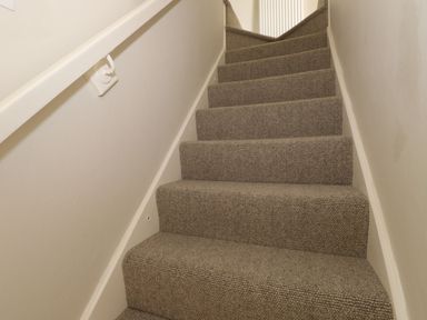 A carpeted staircase with a white handrail and beige walls at Little Robin Cottage in Ambleside