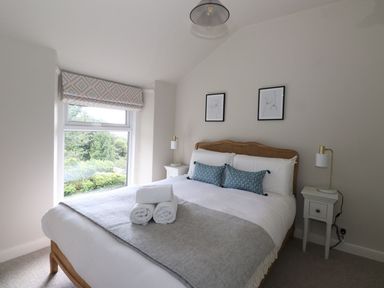 A bedroom with a bed with white linens and blue pillows two bedside tables with lamps and a window with a patterned blind at Little Robin Cottage in Ambleside