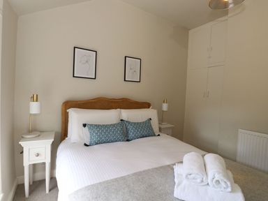 A bedroom with a double bed two blue pillows two bedside tables with lamps folded towels on the bed and built-in wardrobes at Little Robin Cottage in Ambleside