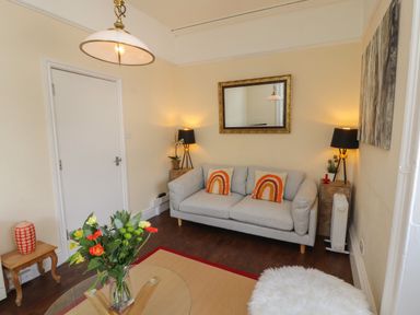 A living room with a grey sofa two orange pillows a mirror and flowers on a glass table at Belmont House in Bowness-On-Windermere