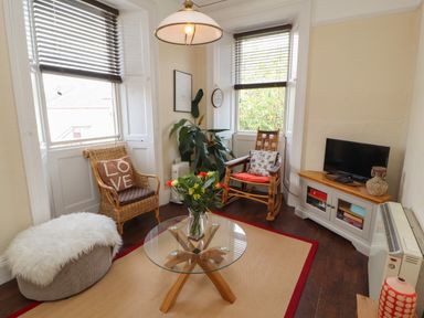 A sitting room with two chairs a glass coffee table a television on a wooden cabinet and a plant at Belmont House in Bowness-On-Windermere