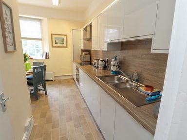 A kitchen with white cabinets wooden countertops a double sink and a small dining area by the window at Belmont House in Bowness-On-Windermere