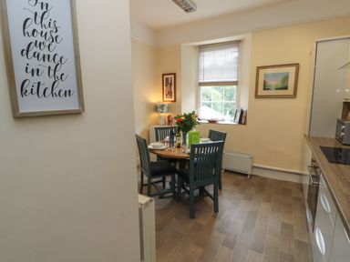 A kitchen dining area with a round table set with four chairs and flowers on the table in a room with a window and framed pictures Belmont House Bowness-On-Windermere