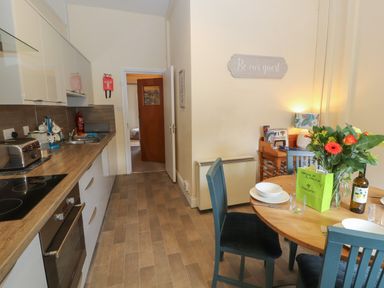 A kitchen with wooden countertop and dining table with chairs flowers and tableware at Belmont House in Bowness-On-Windermere