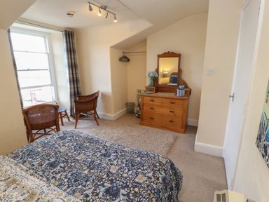 A bedroom with a bed a wooden dresser with a mirror two wicker chairs and a window at Belmont House in Bowness-On-Windermere