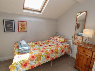 A small bedroom with a single bed with floral bedding towels on the bed a wooden dresser with a lamp and a mirror on the wall at Belmont House in Bowness-On-Windermere