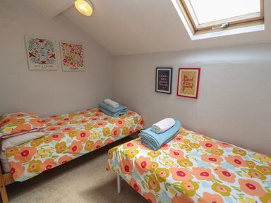 A bedroom with two single beds with floral bedding and framed pictures on the walls at Belmont House in Bowness-On-Windermere
