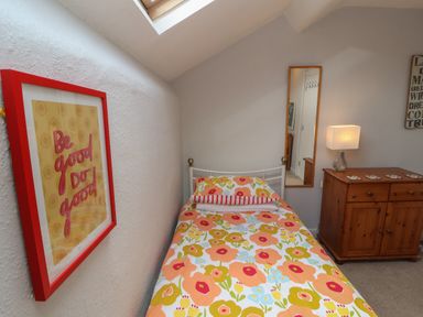 A bedroom with a single bed with floral bedding a bedside cabinet with a lamp a mirror on the wall and a framed poster at Belmont House in Bowness-On-Windermere