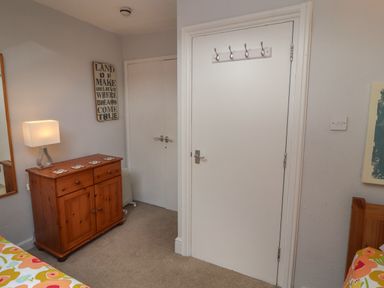 A bedroom corner with a wooden dresser and lamp next to two white doors at Belmont House in Bowness-On-Windermere