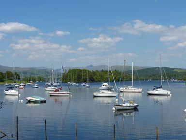 A lake with sailboats and motorboats moored near the shore with hills and trees in the background at Belmont House in Bowness-On-Windermere