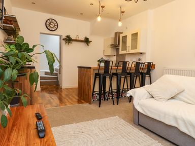A living room with a sofa and kitchen area with bar stools at Hole in the Wall in Caernarfon