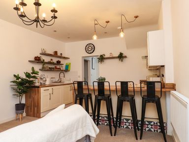 A kitchen with wooden countertops black bar stools shelves with kitchenware and a potted plant at Hole in the Wall in Caernarfon