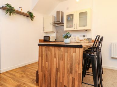 A kitchen with a wooden island and black bar stools at Hole in the Wall in Caernarfon