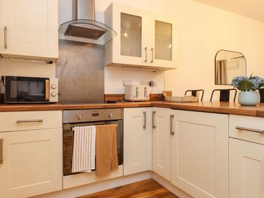 A kitchen with white cabinets a built in oven microwave toaster a wicker basket and a flower vase at Hole in the Wall in Caernarfon