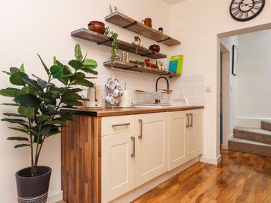 A kitchen with cream cabinets wooden shelves and a potted plant at Hole in the Wall in Caernarfon