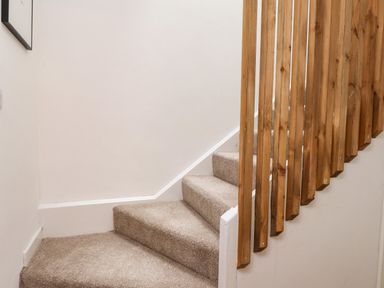 A carpeted staircase with wooden vertical railings at Hole in the Wall in Caernarfon